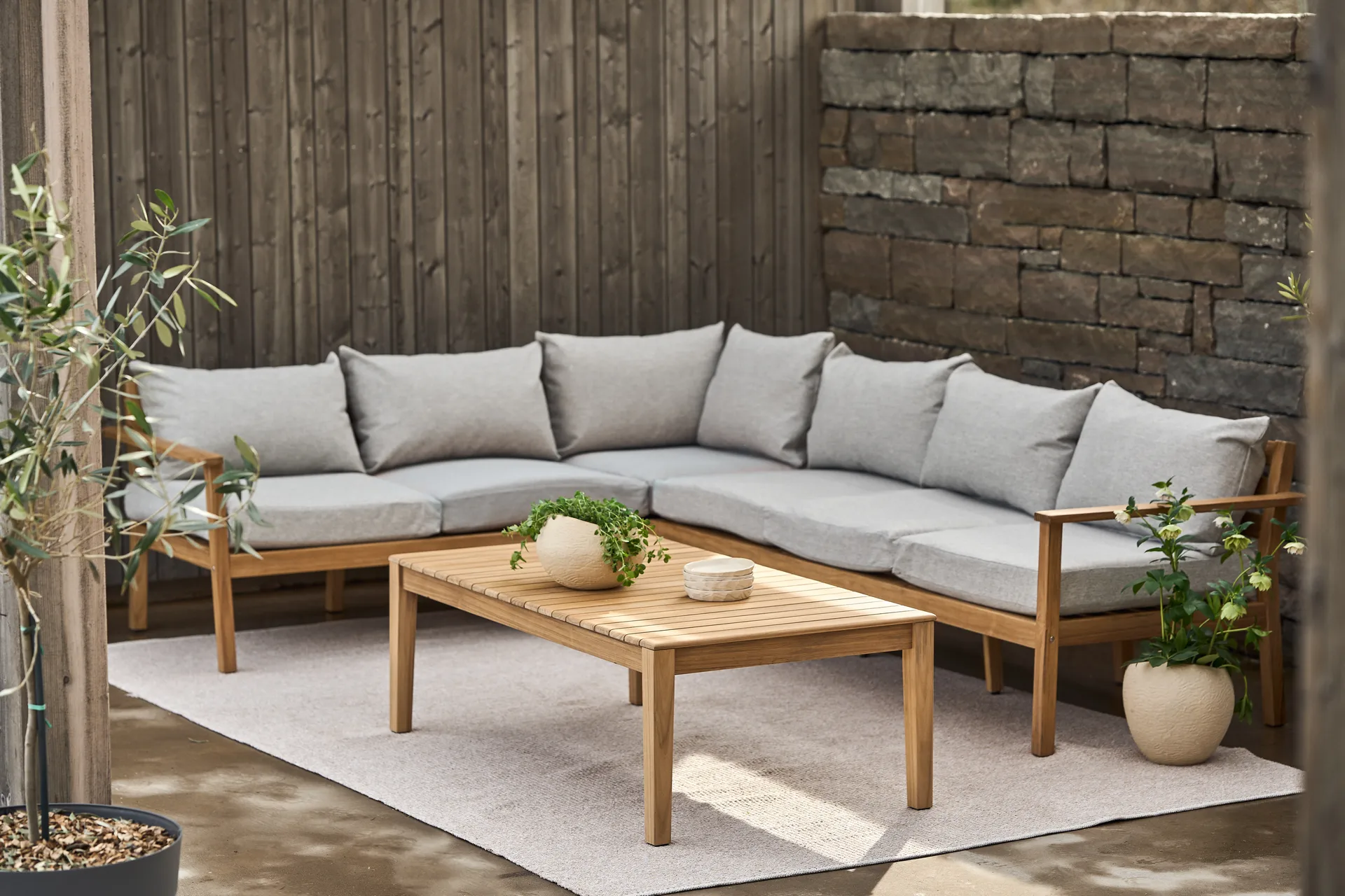 L-shaped wooden outdoor sofa with gray cushions and a slatted coffee table on a patio rug.