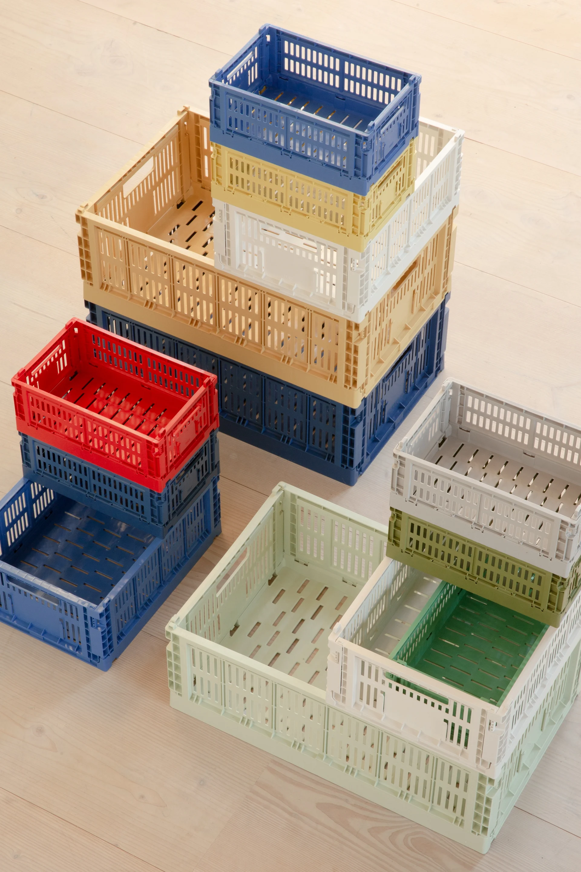Stacks of colorful, perforated plastic folding crates on a light wooden floor.