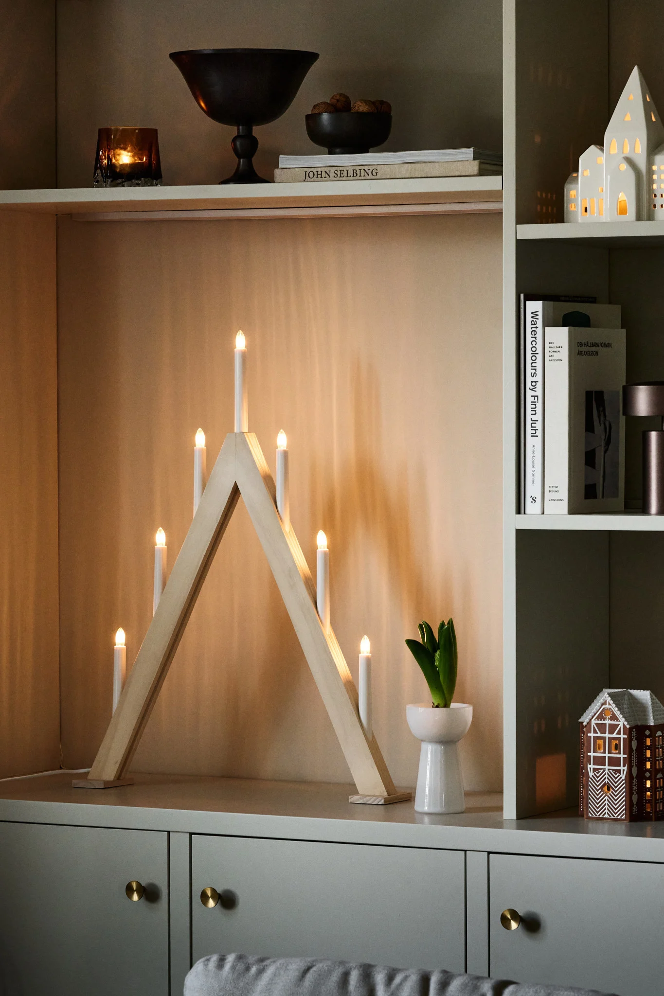 A pointed Advent candle holder stands on a chest of drawers and shines beautifully alongside other Christmas decorations.