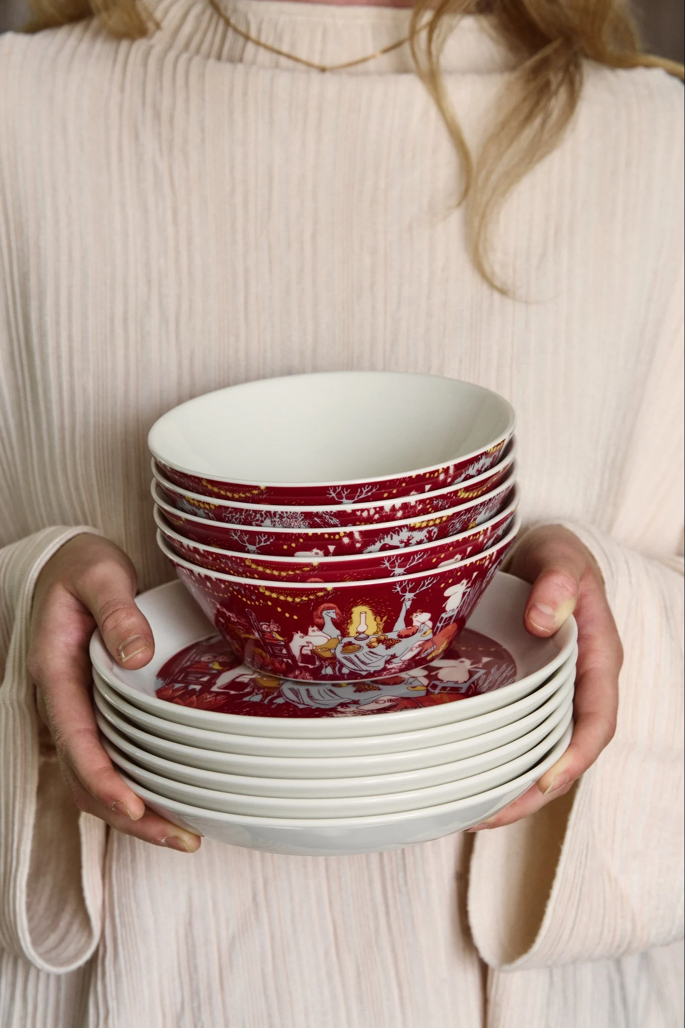 A person holding a stack of red, illustrated bowls with white interiors, and a stack of white plates underneath.