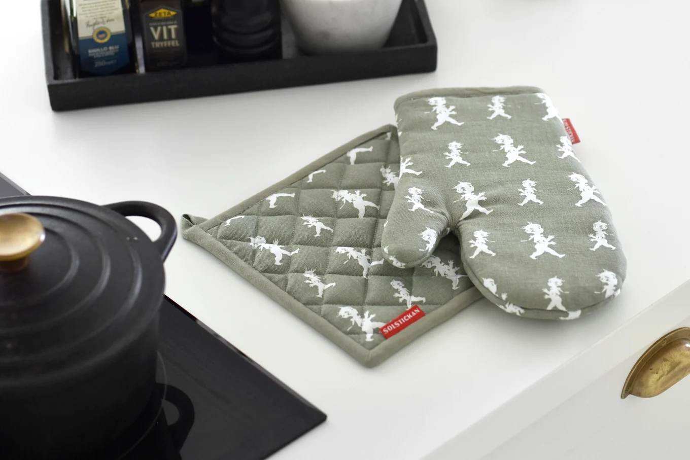 Green oven mitt and pot holder with white gnome pattern on a kitchen counter next to a black pot.