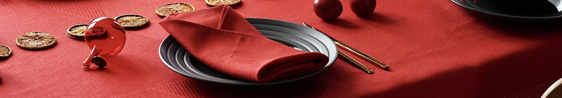 Table set with a red tablecloth, dark plate, red napkin, gold chopsticks, and dried orange slices.