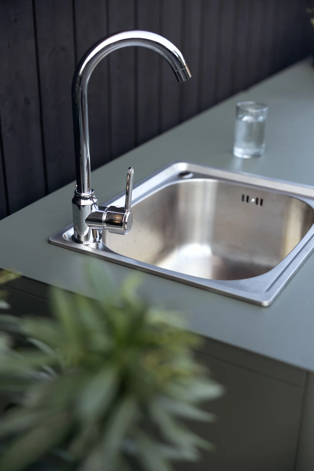 Outdoor kitchen sink with a chrome faucet and a glass of water on a green countertop.