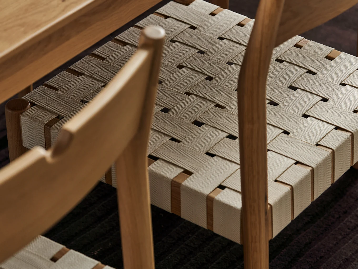 Close-up of a light wood chair seat with beige woven fabric straps in a herringbone pattern.
