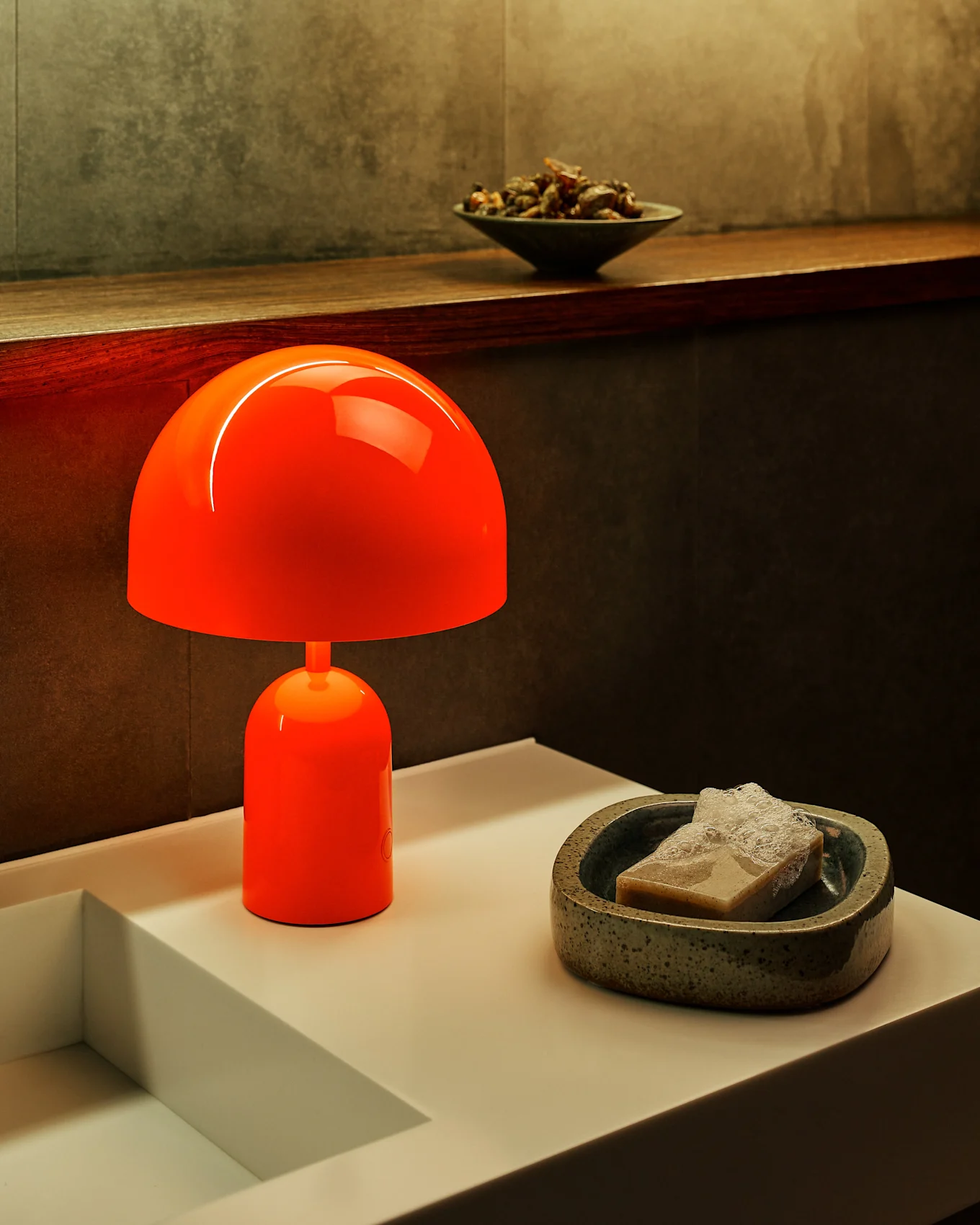 Vibrant orange mushroom lamp on a white counter next to a sink, with a bar of soap in a speckled dish.