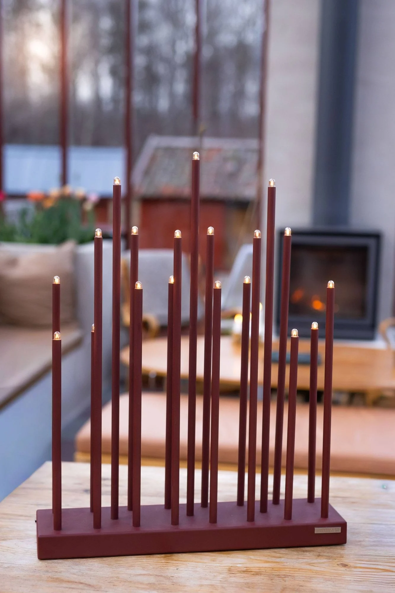 A modern dark red light decoration featuring several vertical rods of different lengths with illuminated tips, on a wooden table.