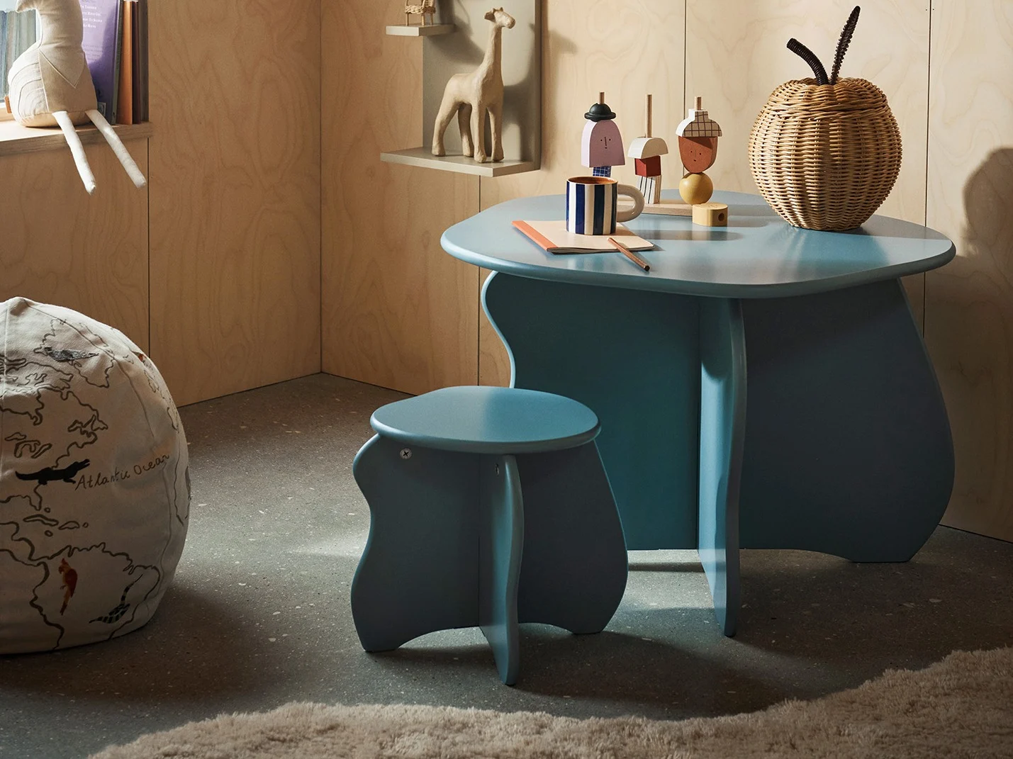 A child's room with a light blue table and stool, a world map bean bag, and wooden toys on shelves.