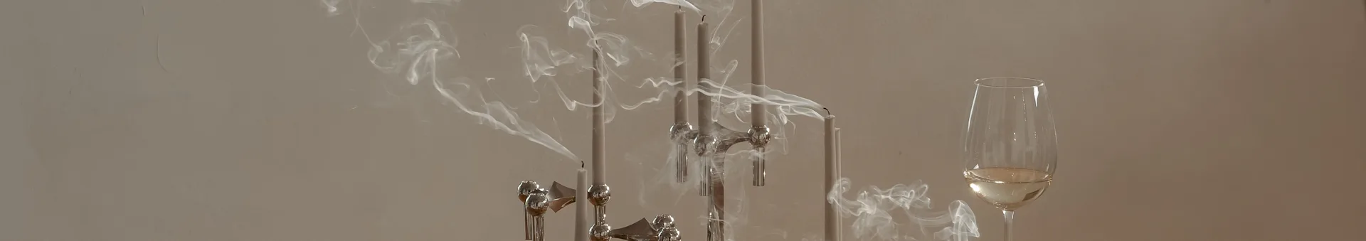 Smoke rising from extinguished slender grey candles in a silver candelabra, next to a glass of white wine.