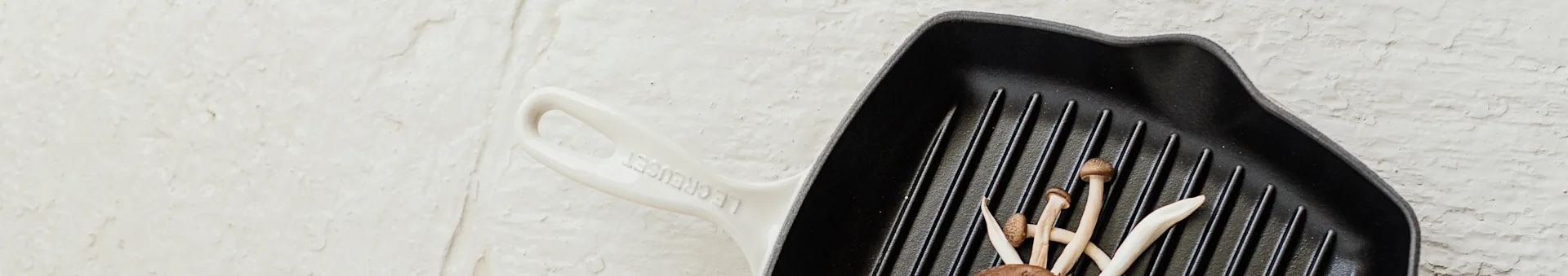 Mushrooms in a black cast iron grill pan with an off-white handle on a textured white surface.