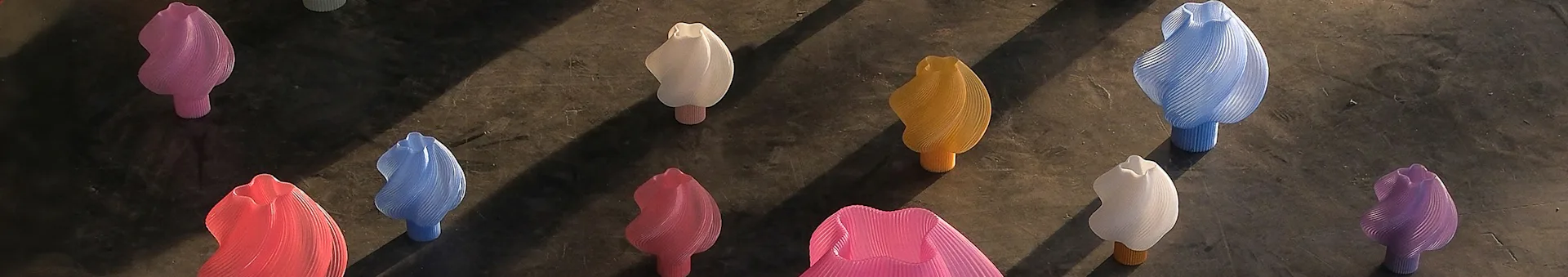 A row of abstract, ribbed, flower-like objects in pink, white, yellow, blue, red, and purple on a dark surface.