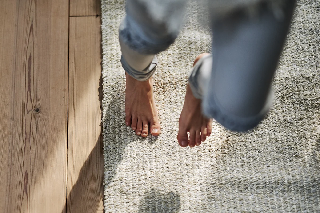 Bare feet standing on a light-colored rug, with a wooden floor visible to the left.