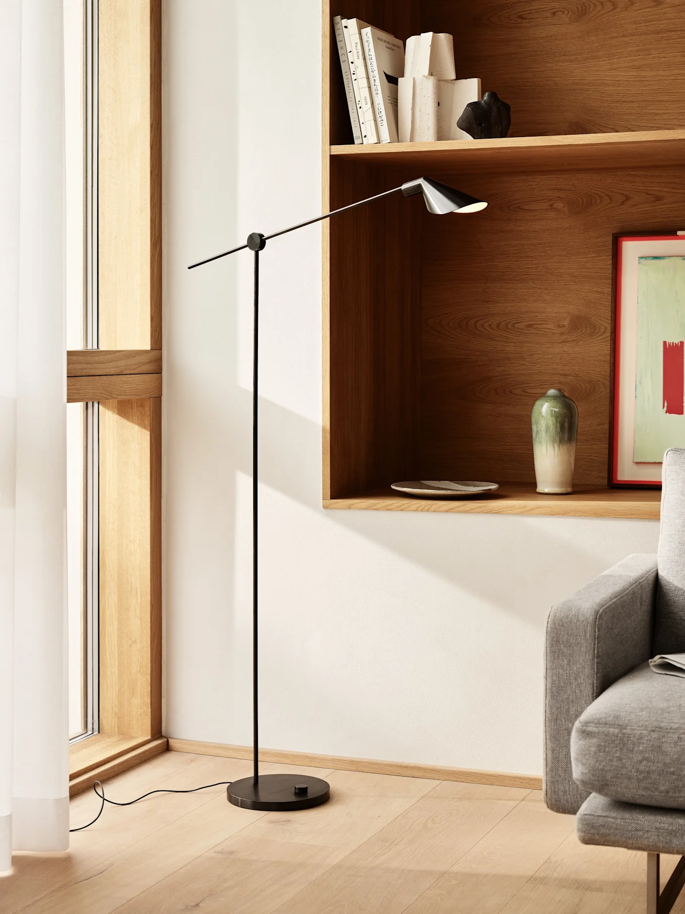 Tall, slender black floor lamp with an adjustable arm and dark shade in a modern living space with wooden shelves.