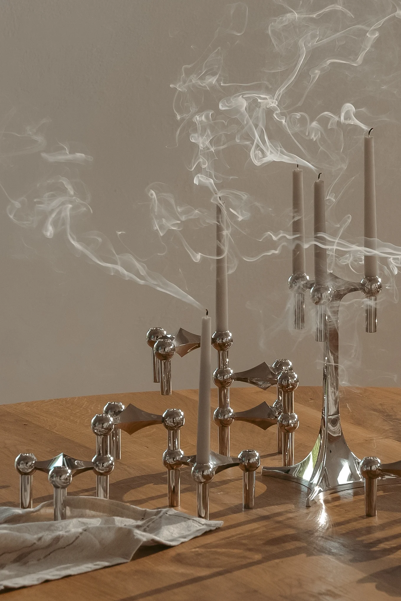 Silver modular candle holders with extinguished candles emitting smoke on a wooden table.
