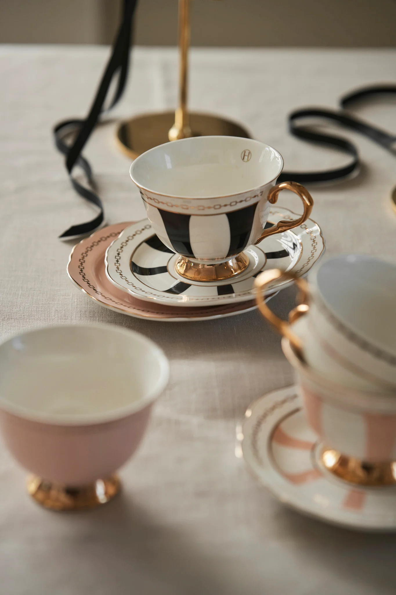 Elegant teacup and saucers, the main cup with black and white stripes and gold accents, on a light tablecloth.