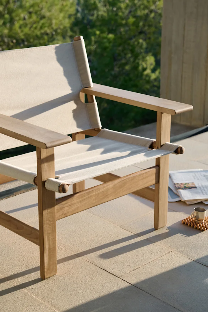 Light wooden outdoor chair with cream canvas on a patio, with a newspaper and cup beside it.