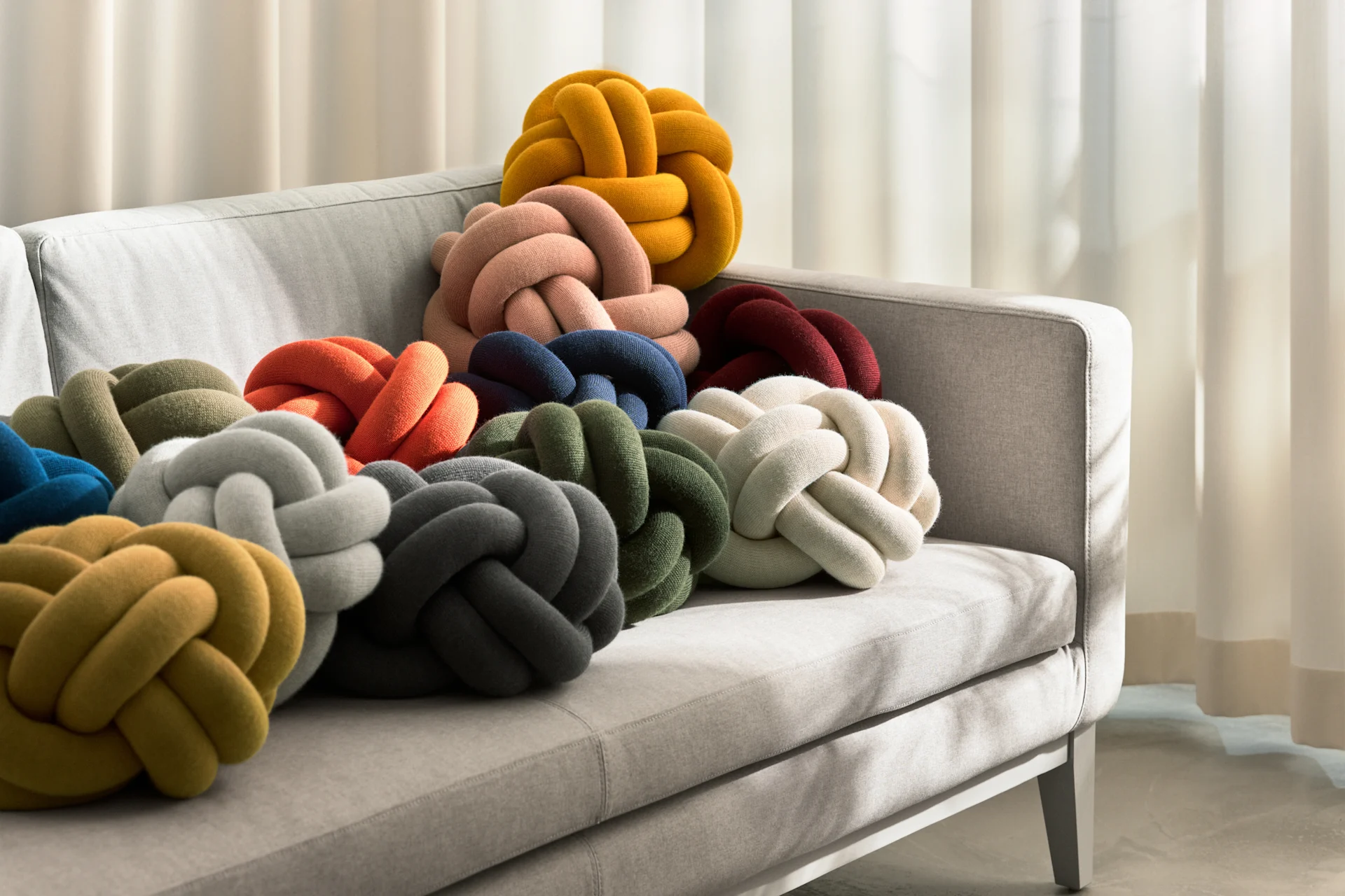 Grey sofa filled with various colorful knot pillows in yellow, peach, blue, red, green, cream, grey, and orange.