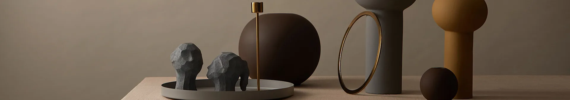 Modern decor: Grey abstract sculptures, gold candle holder, various colored vases, and an oval mirror on wood.
