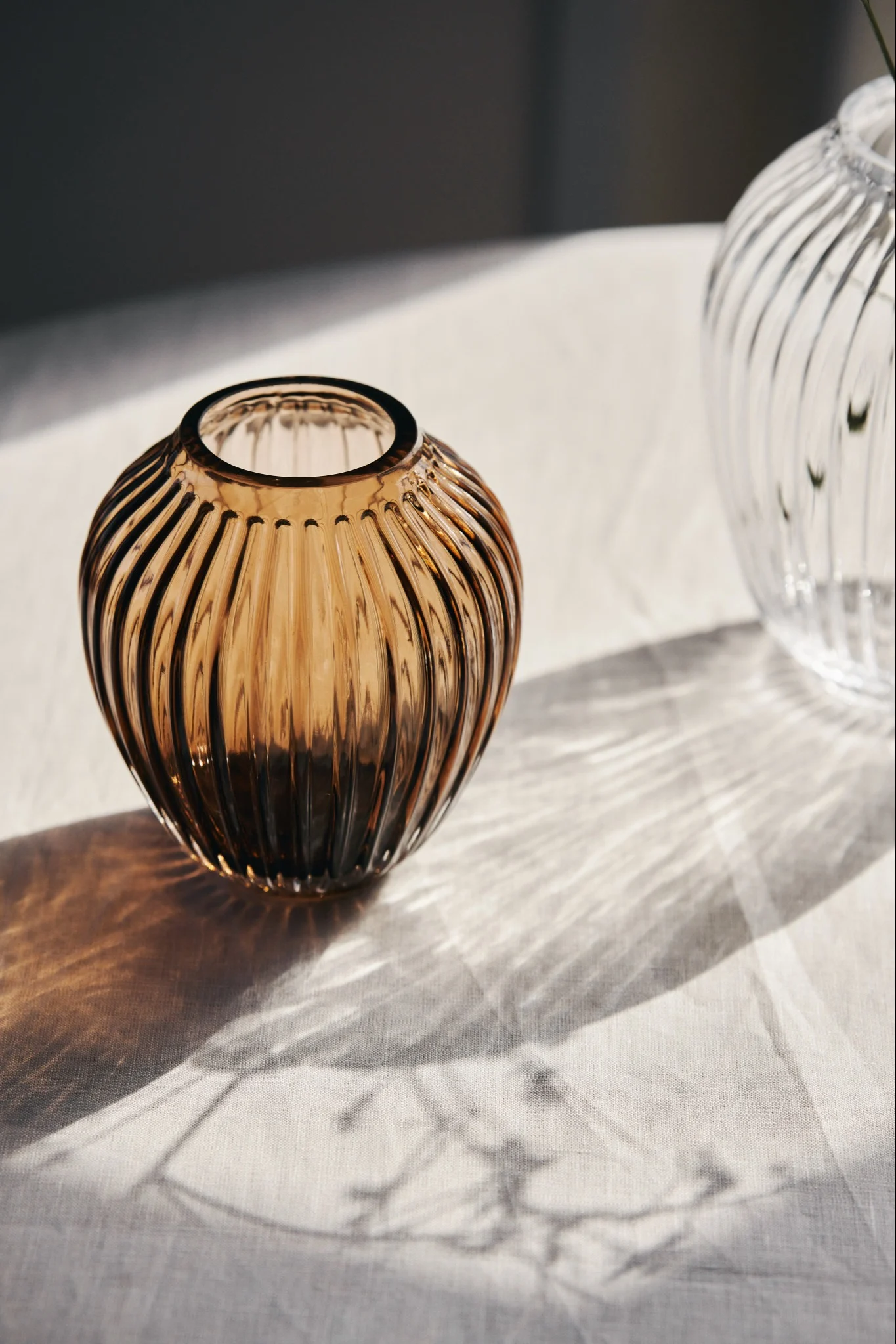 Here you see the sunlight shining through the small glass vase in walnut and the larger clear glass vase from Kähler's Hammershøi collection.