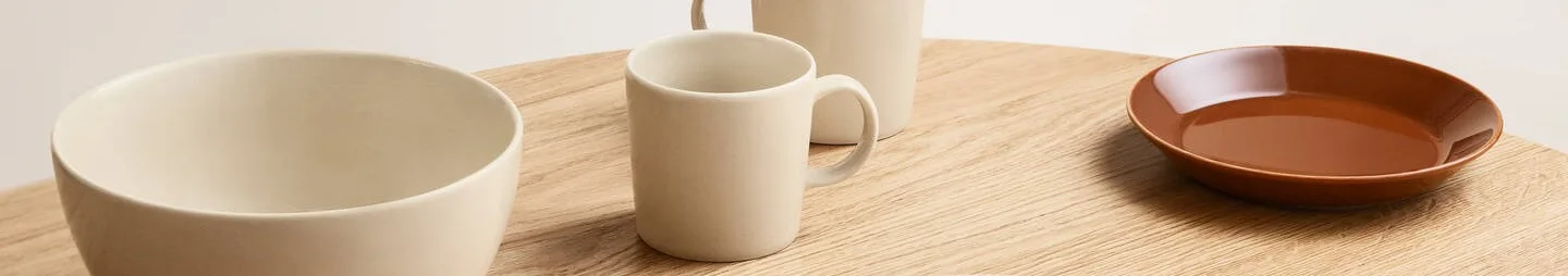 Cream-colored bowl and mugs, and a brown plate on a light wood table.