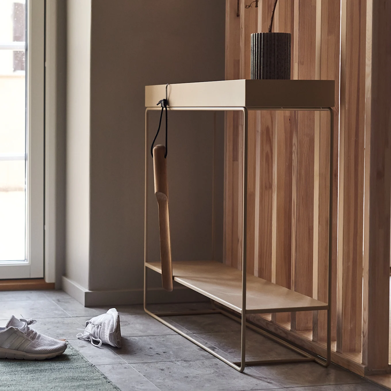 Entryway with a light metal and wood console table, a wooden shoehorn, and two white sneakers on a green rug.