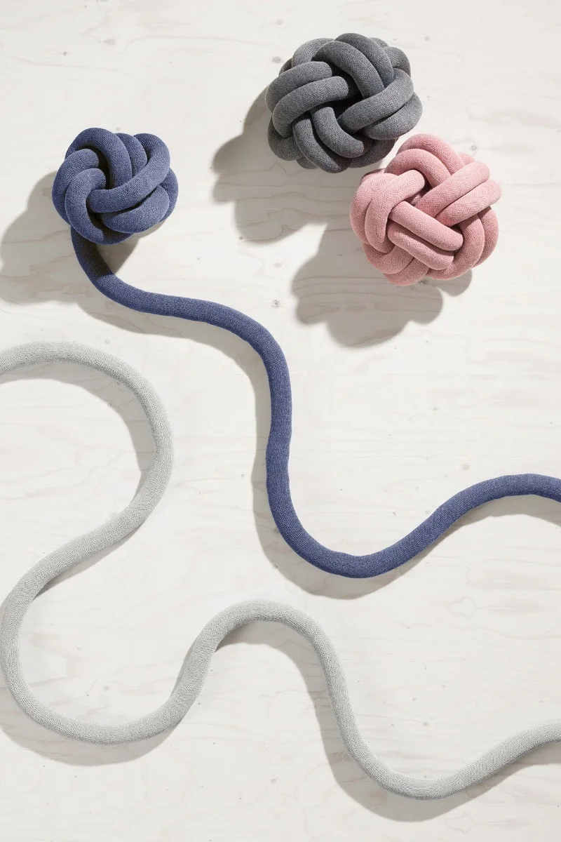 Three knotted cushions in blue, gray, and pink, with blue and gray fabric tubes, on a light wood surface.
