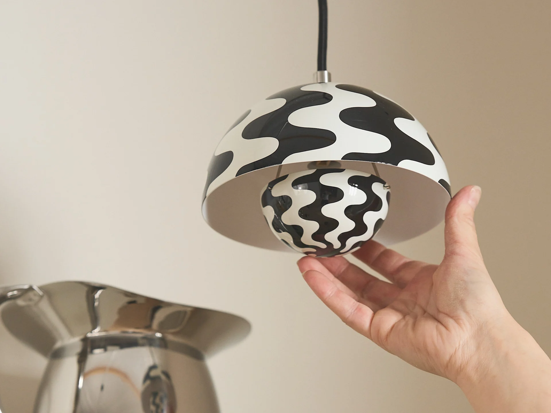 Hand adjusting a pendant lamp with a black and white wavy pattern on both the shade and the spherical bulb.