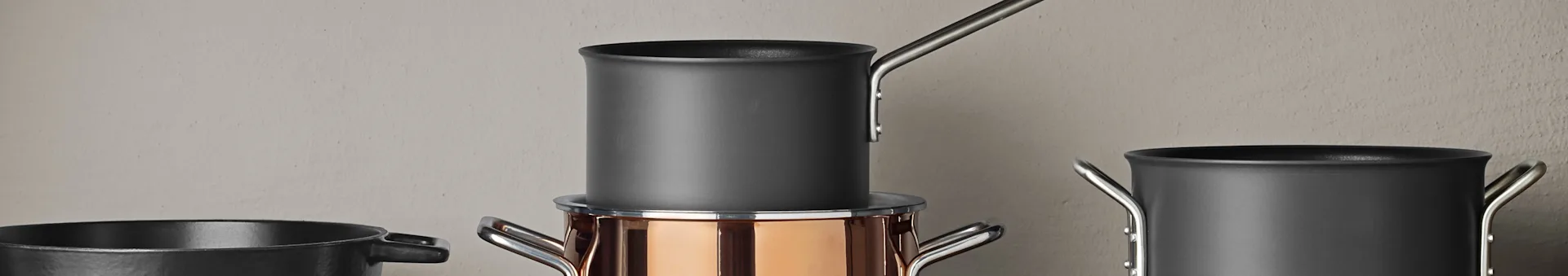 A collection of pots and pans, including a copper-colored pot with a dark gray saucepan stacked on top, and other dark gray pots.