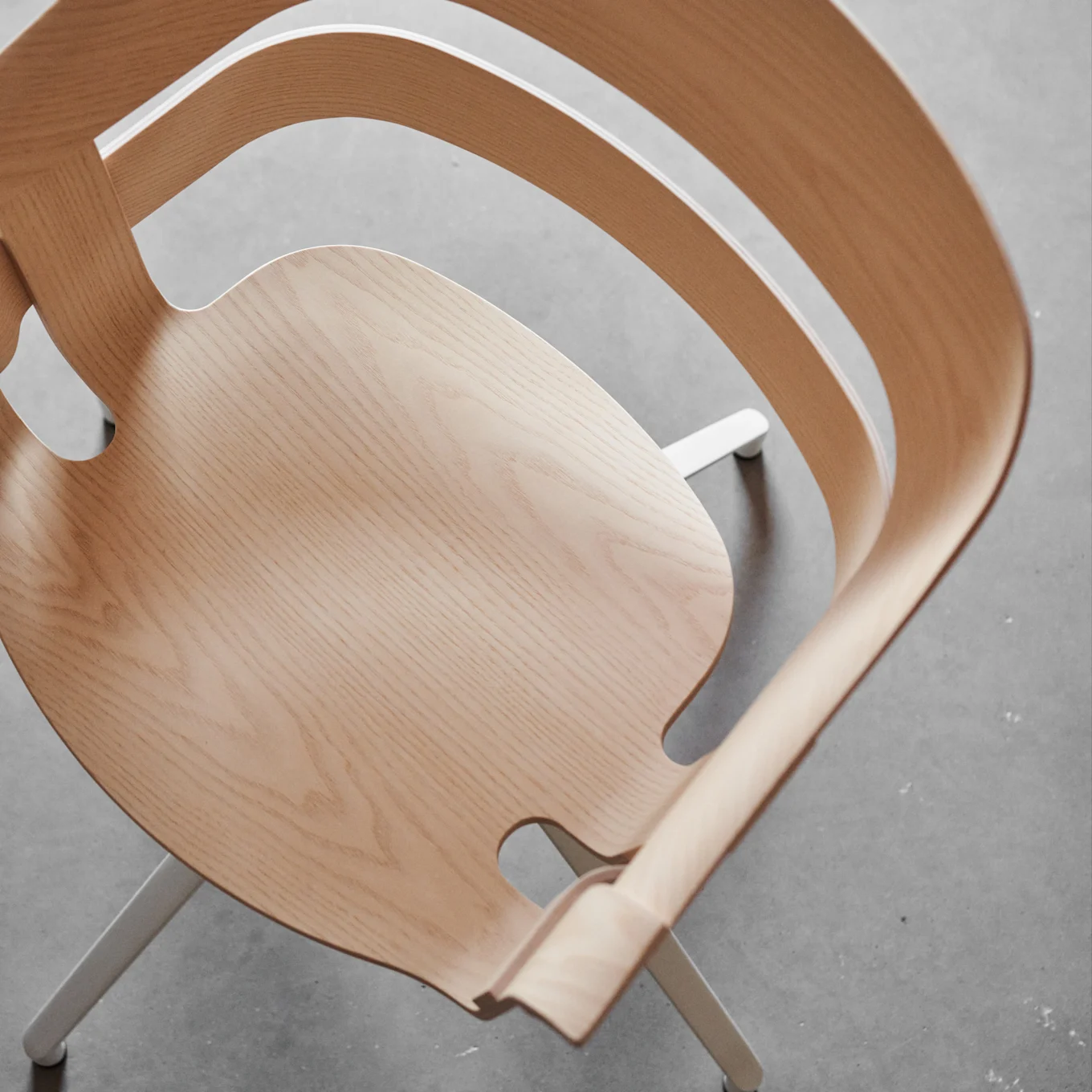 High-angle view of a modern wooden chair with light-colored curved plywood and white metal legs on a concrete floor.