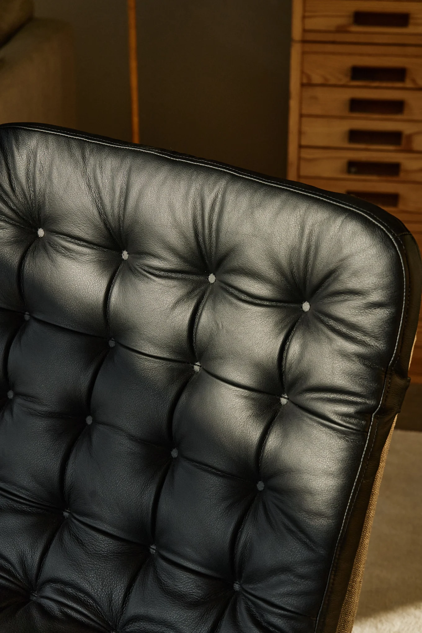 Close-up of a black leather tufted armchair backrest, showing textured leather and buttons.