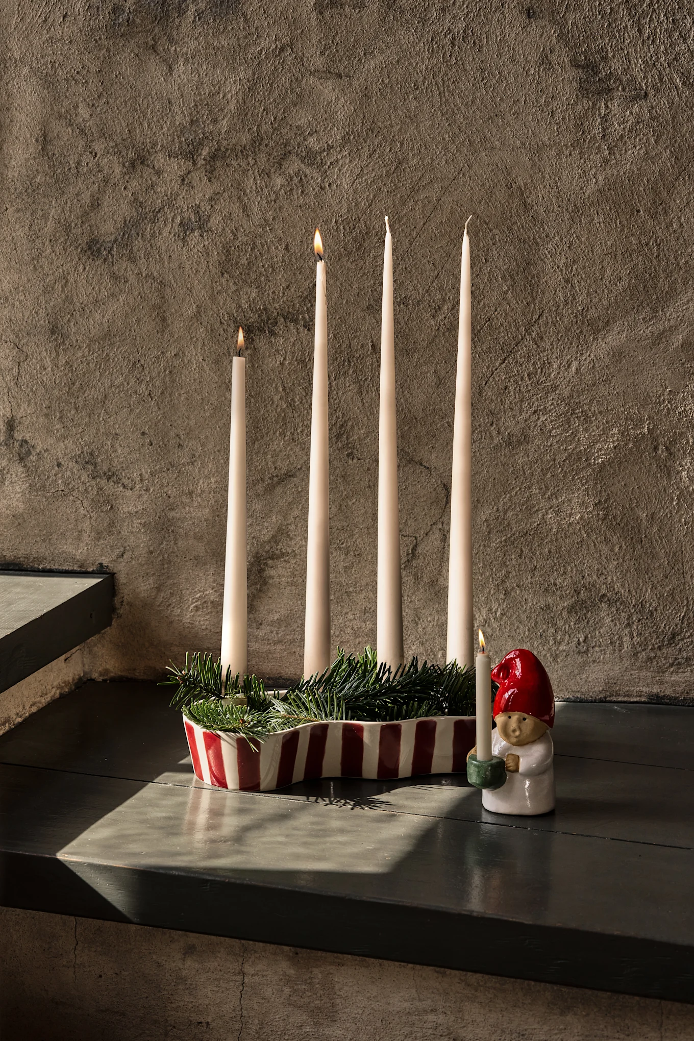 Elegant table set with dark red cloth, wine glasses, plates, a tiered fruit stand, and lit candles.