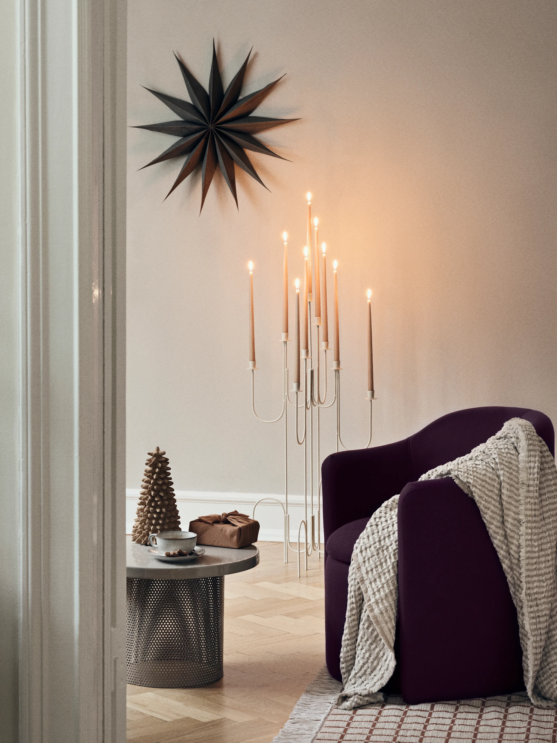A bright winter scene through a window, with snowy trees and a sunburst. Inside, a table with candles and paper trees, and a paper star hangs in the window.