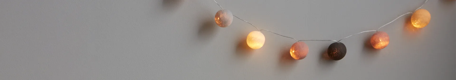 String of spherical decorative lights in beige, white, pink, dark brown, and orange against a grey wall.