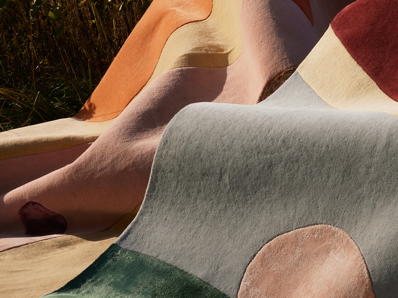 Colorful rugs with wavy, organic shapes and patterns, draped outdoors.