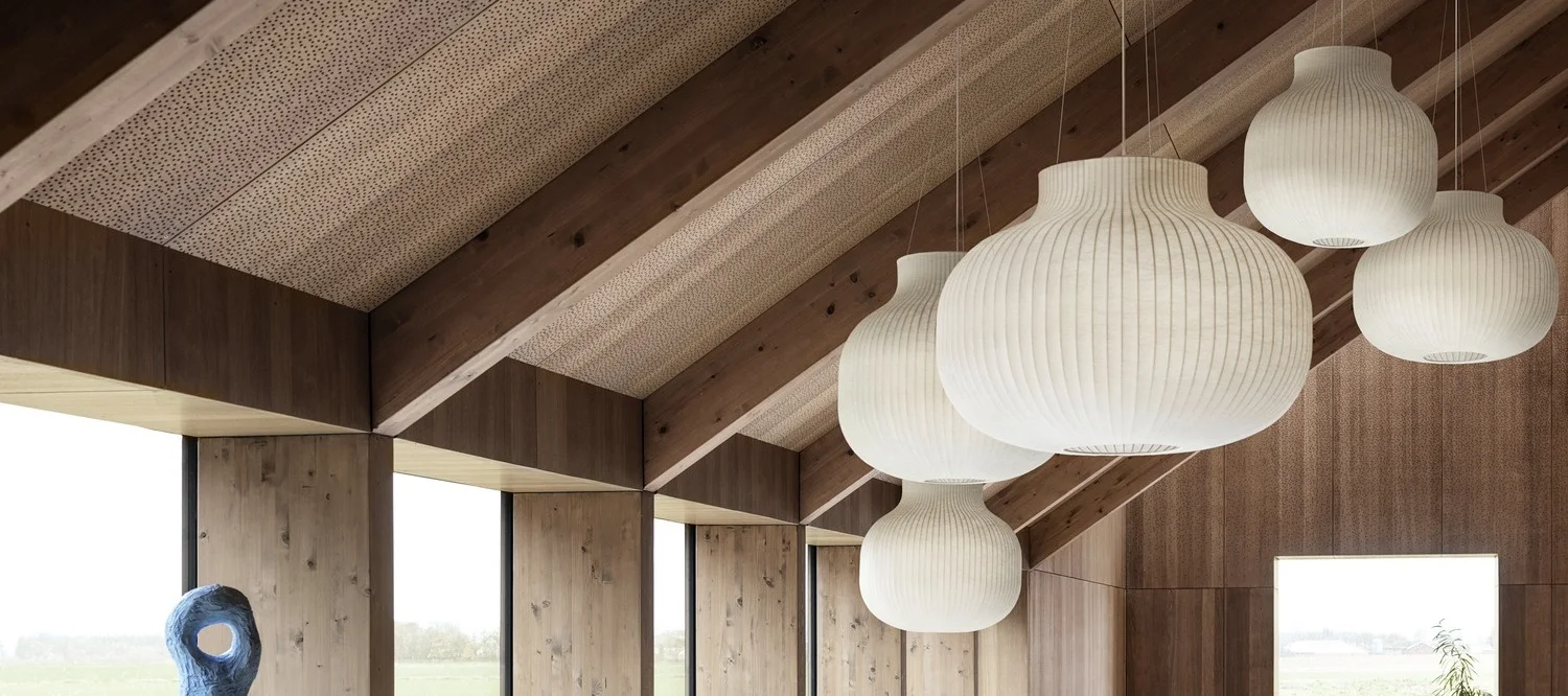 Modern room with vaulted wooden ceiling and large windows, featuring several white, ribbed pendant lamps.