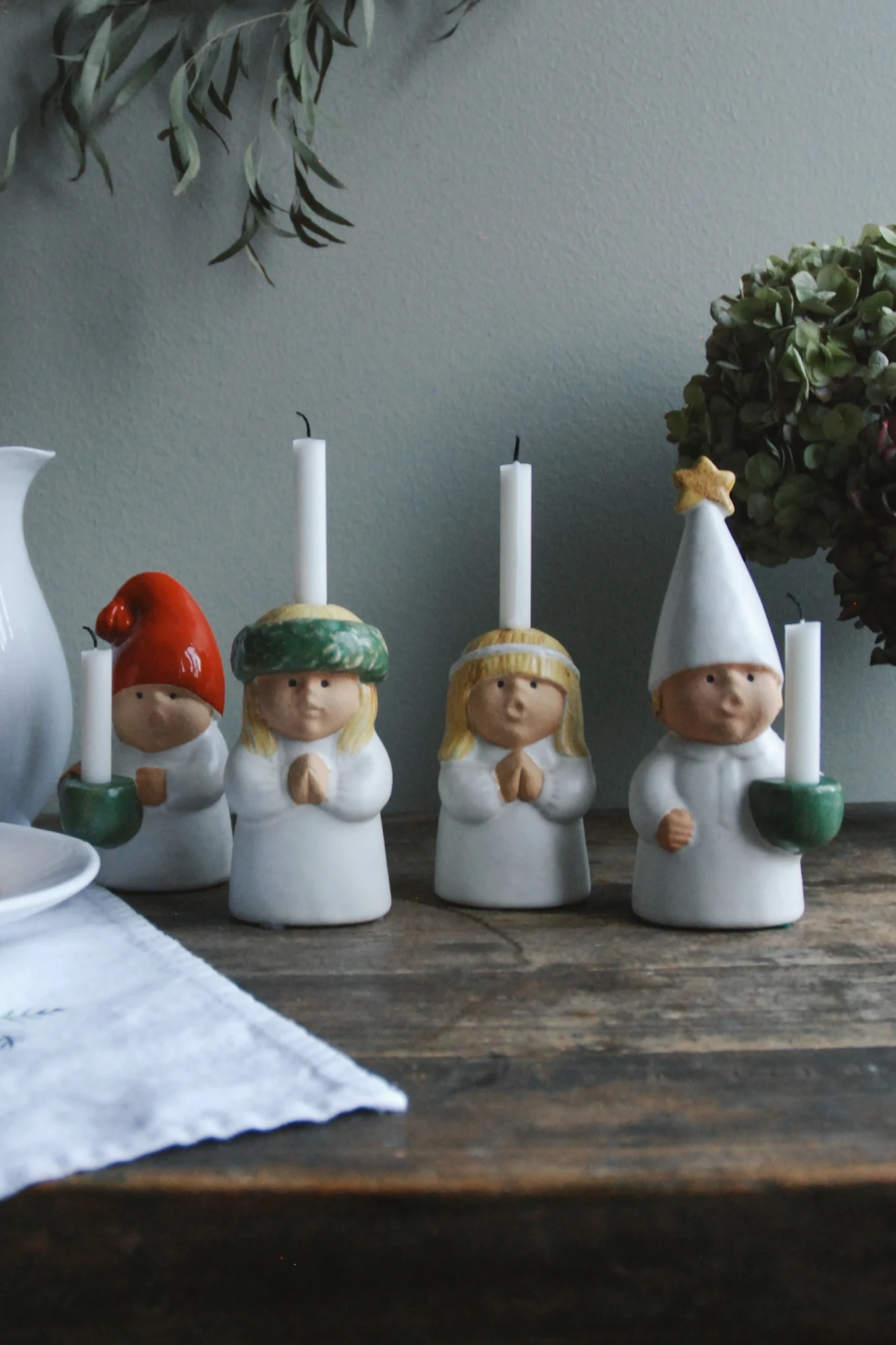 Four festive ceramic figures, two with candles on their heads and two holding candles, on a rustic wooden table.