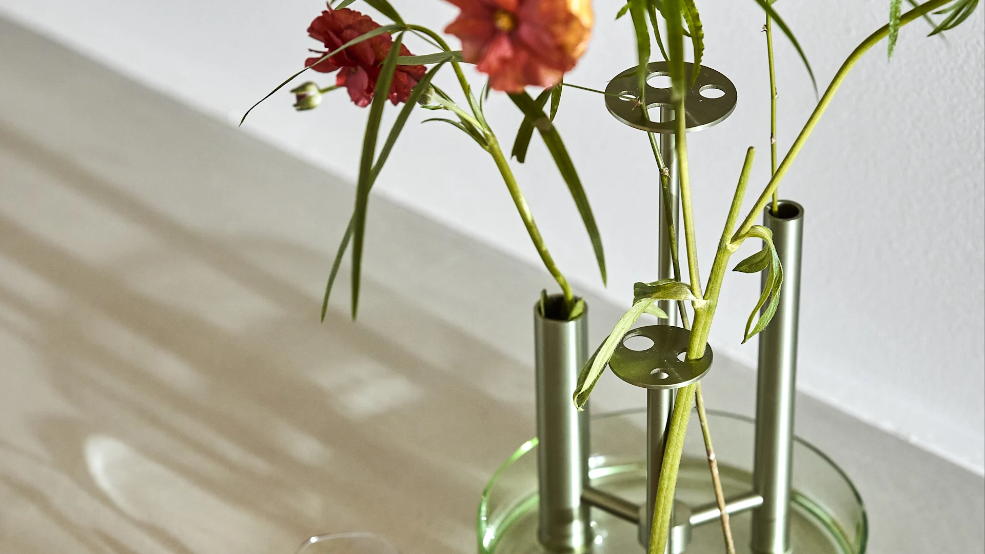 Close-up of a modern vase with red flowers, featuring a green glass base and silver components.