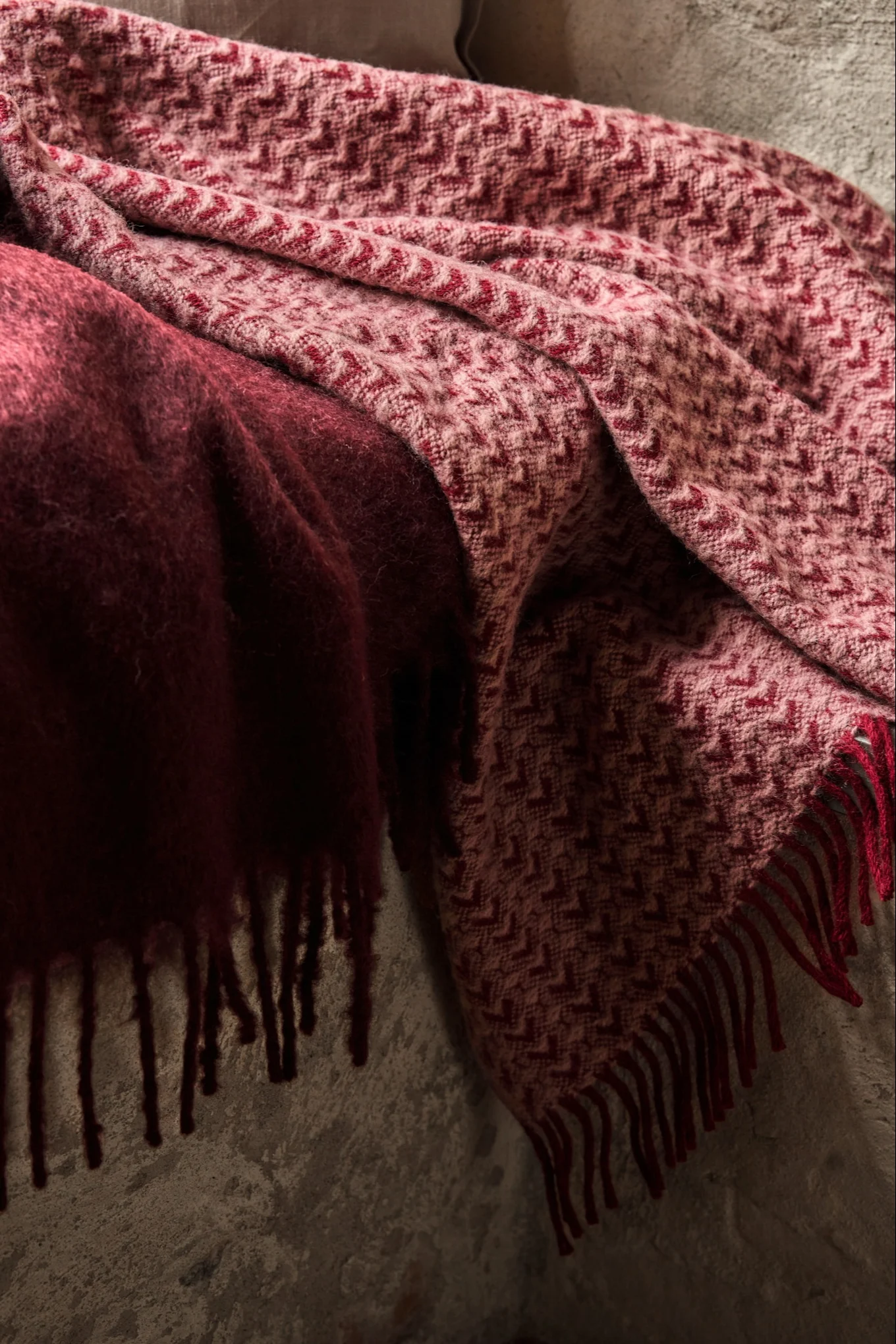 Two throws, one fuzzy dark red and one light red with a chevron pattern and fringe, draped over a surface.