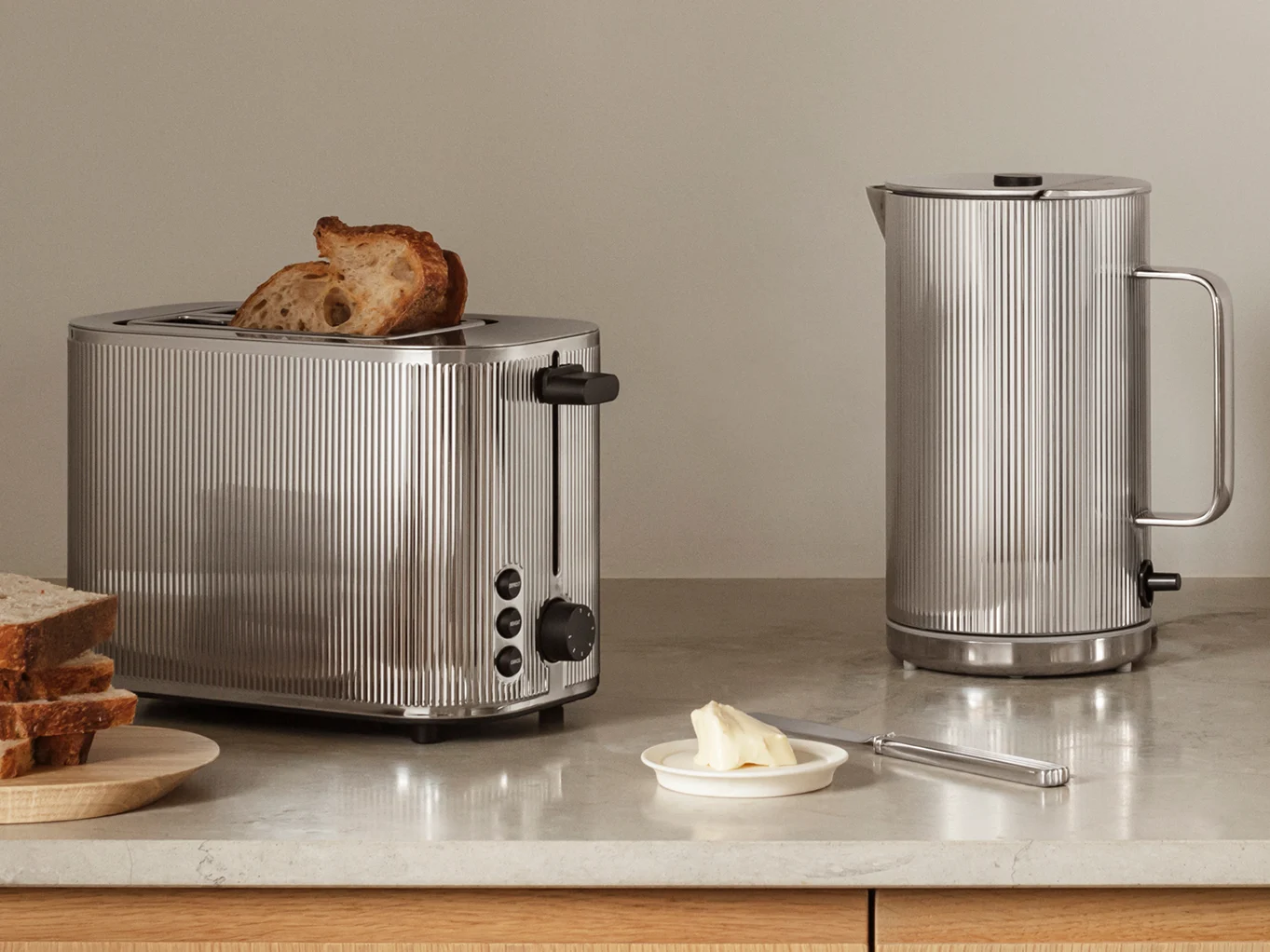 Chrome-plated toaster with toast and matching kettle on a kitchen counter, alongside bread and butter.