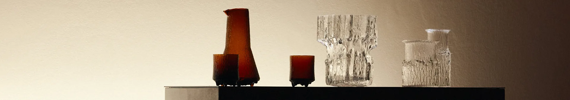A collection of textured glass vases and bottles, amber and clear, on a dark surface against a light background.