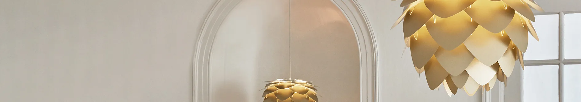 Two golden, layered pendant lights, one in foreground and one in an arched wall niche.