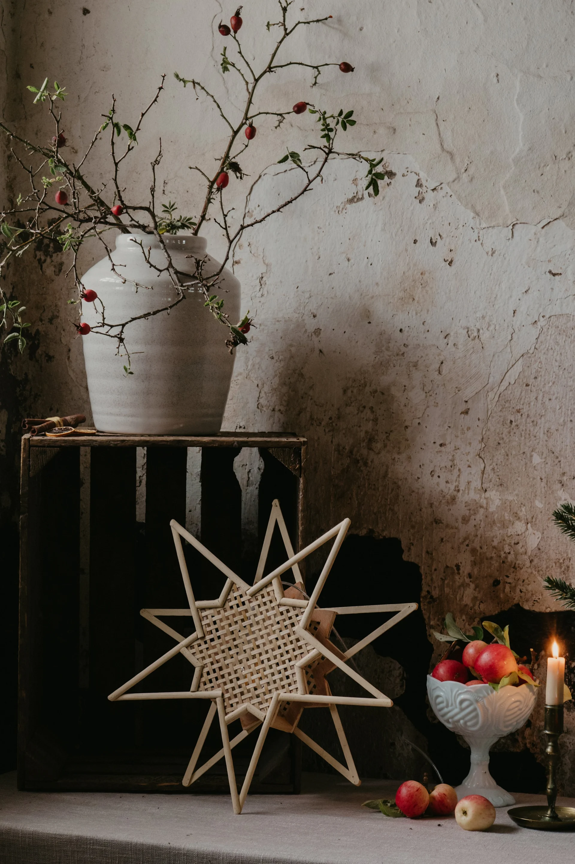 A star-shaped light fixture hangs in front of a window, above a tufted window seat with candles, a mug, and pastries.