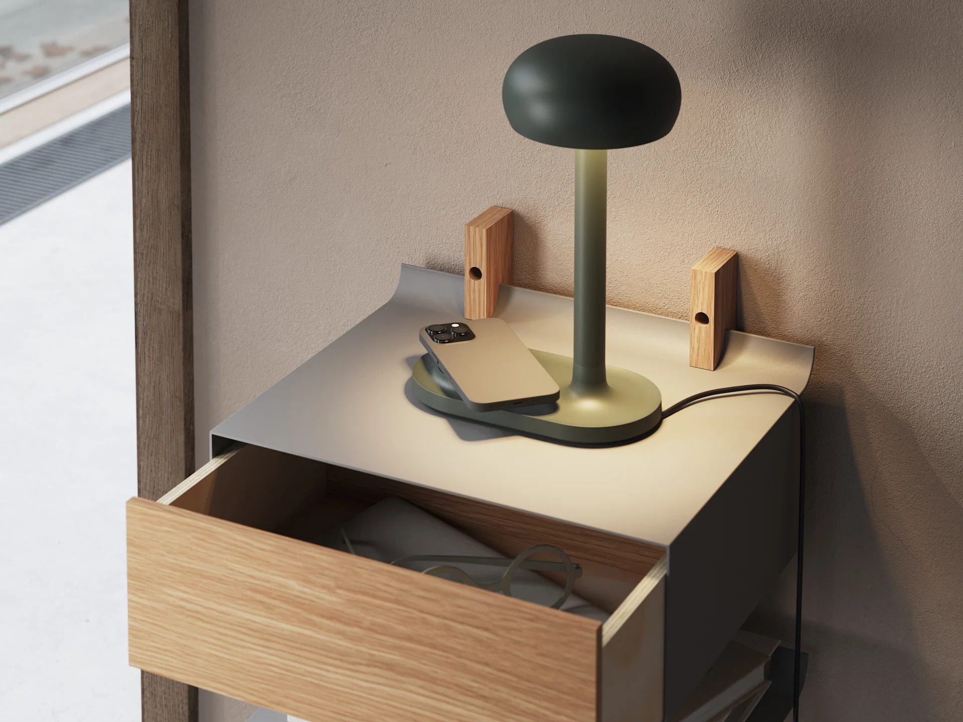 A dark green mushroom lamp, a smartphone on a charging pad, and eyeglasses in an open drawer of a metal and wood bedside table.