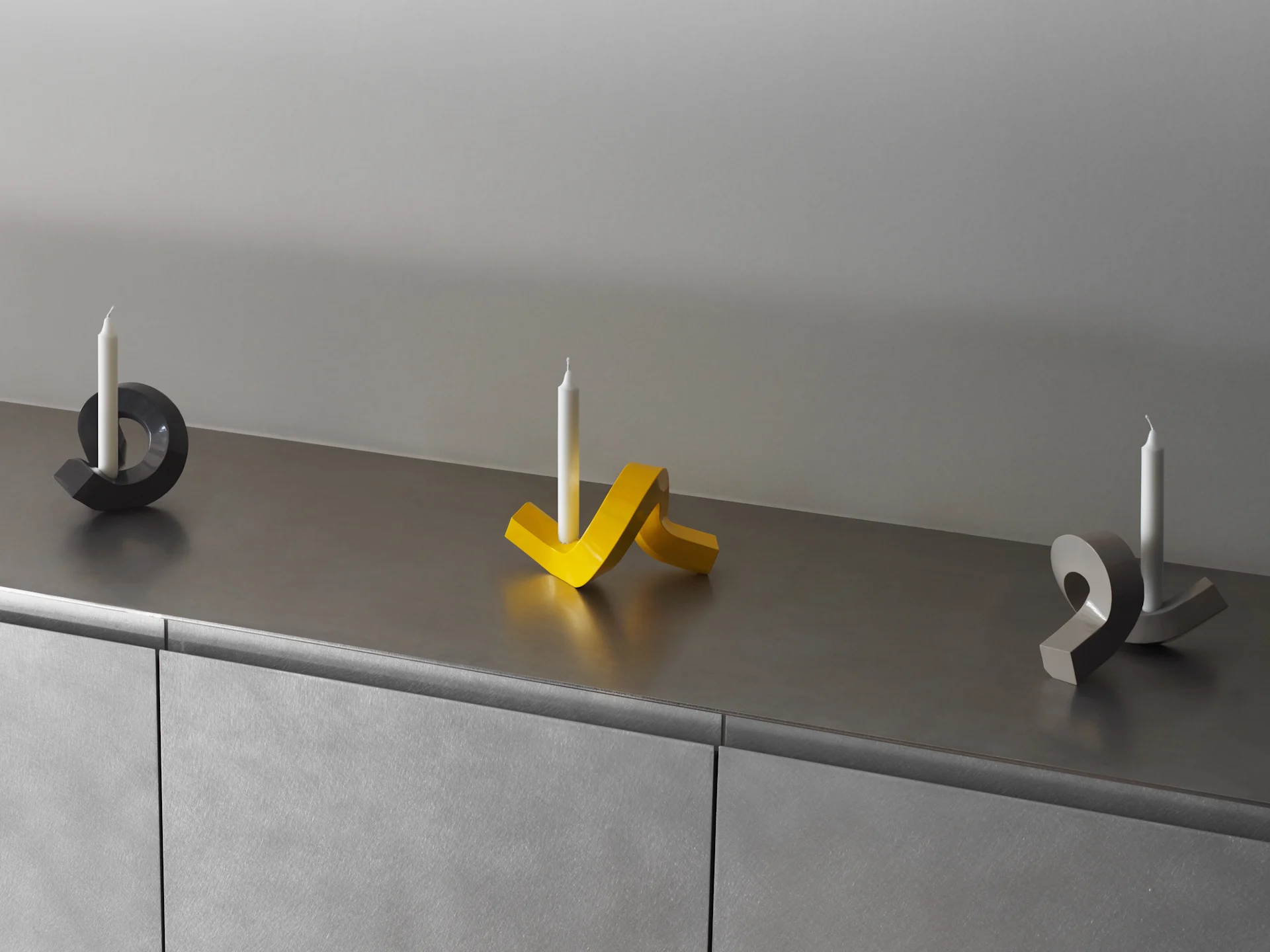 Three modern, sculptural candle holders with white candles on a gray surface.