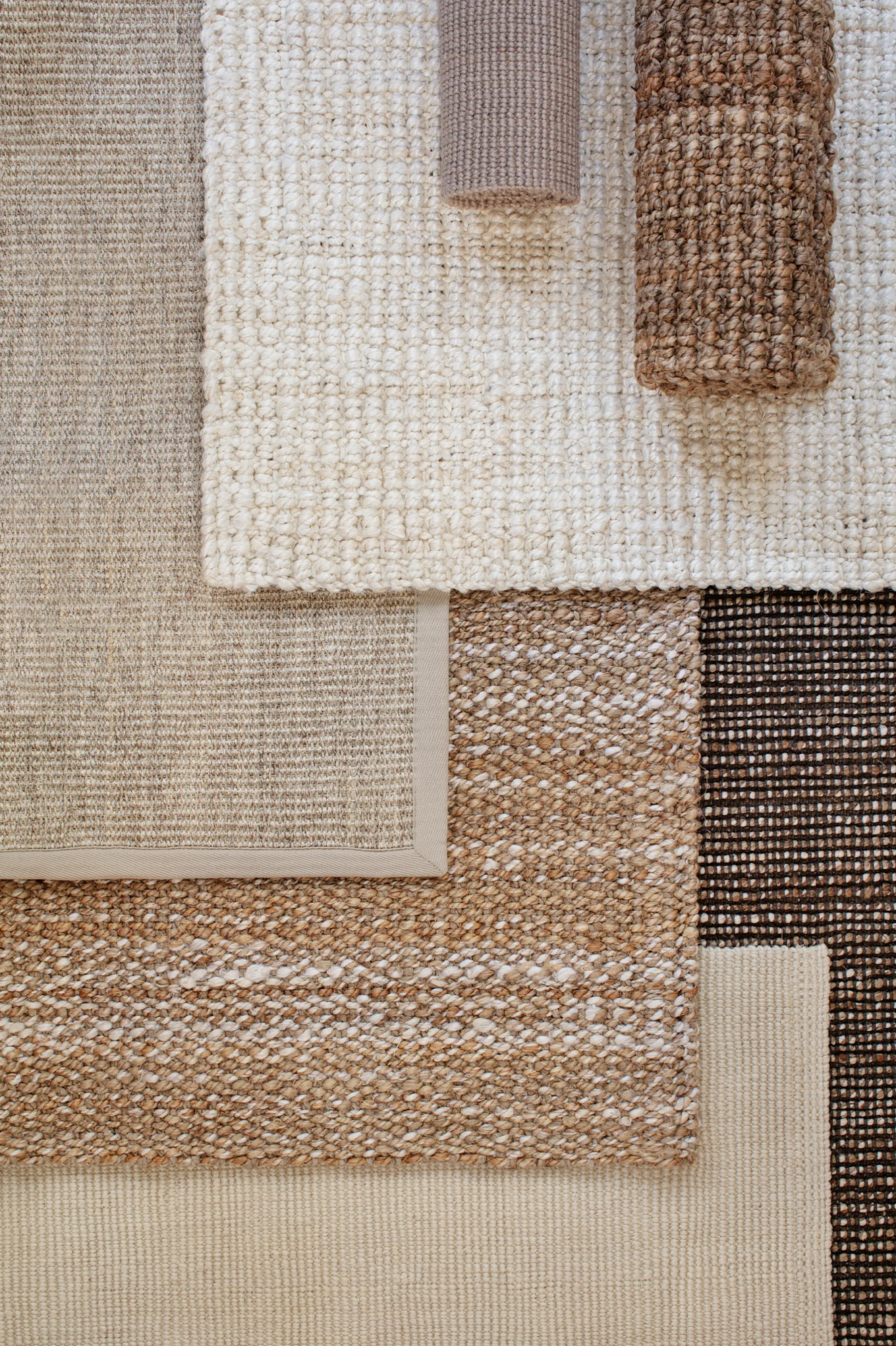 Overlapping natural fiber rugs in shades of beige, cream, and brown, with varied textures.