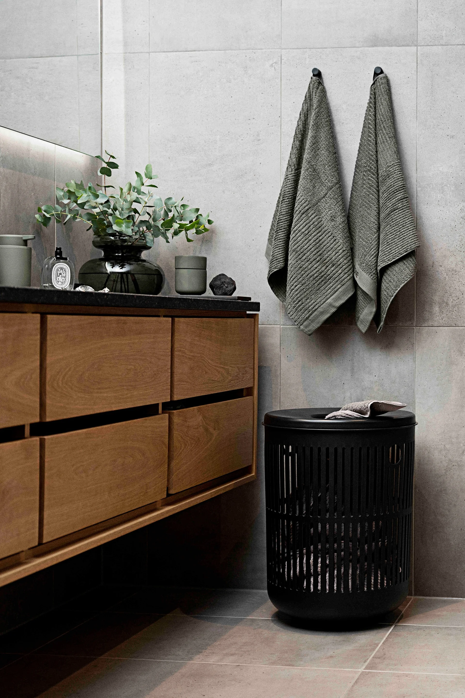 Modern bathroom with a wooden vanity, a plant, and two grey towels hanging next to a black laundry basket.