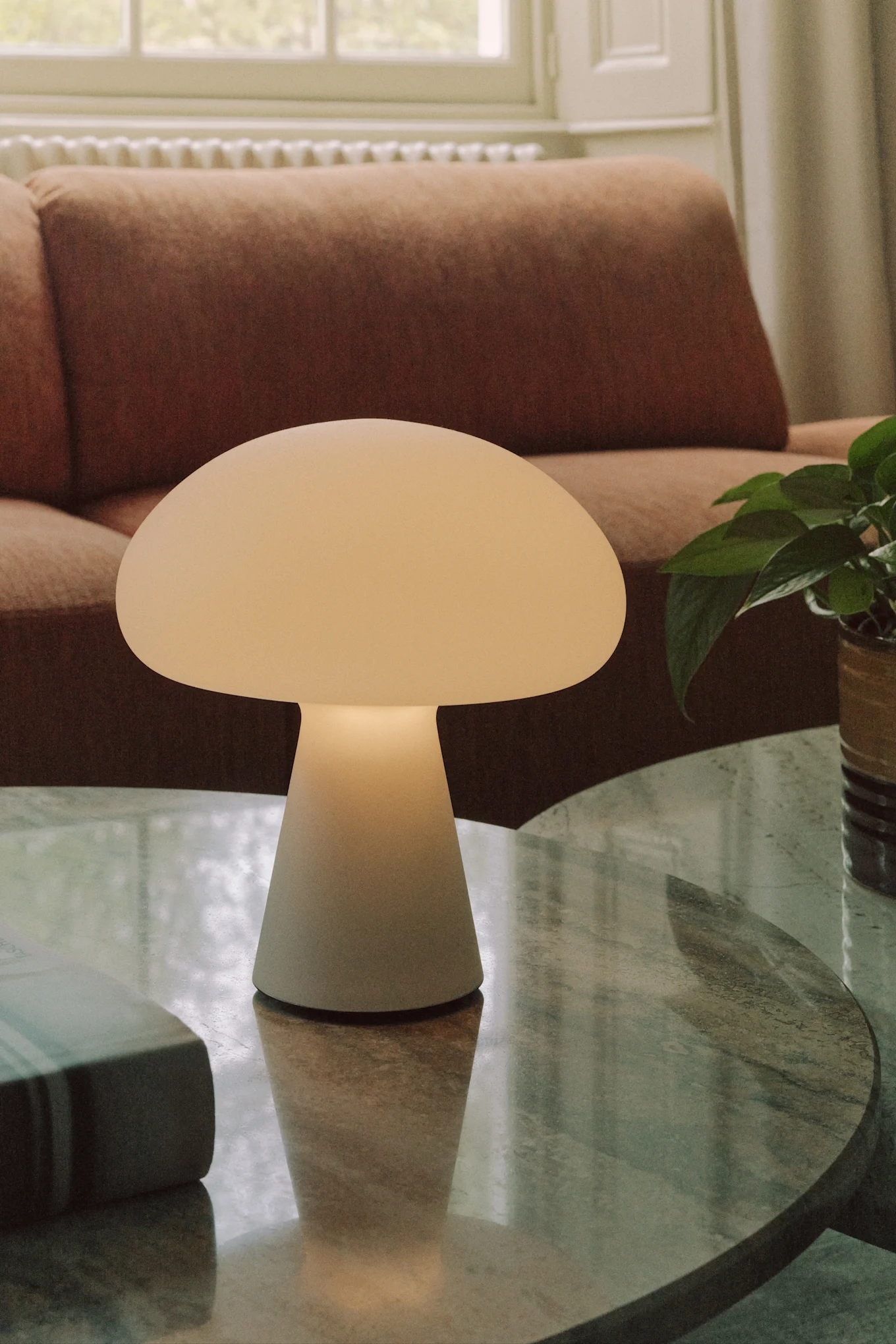 Mushroom-shaped table lamp on a marble table with a sofa in the background.