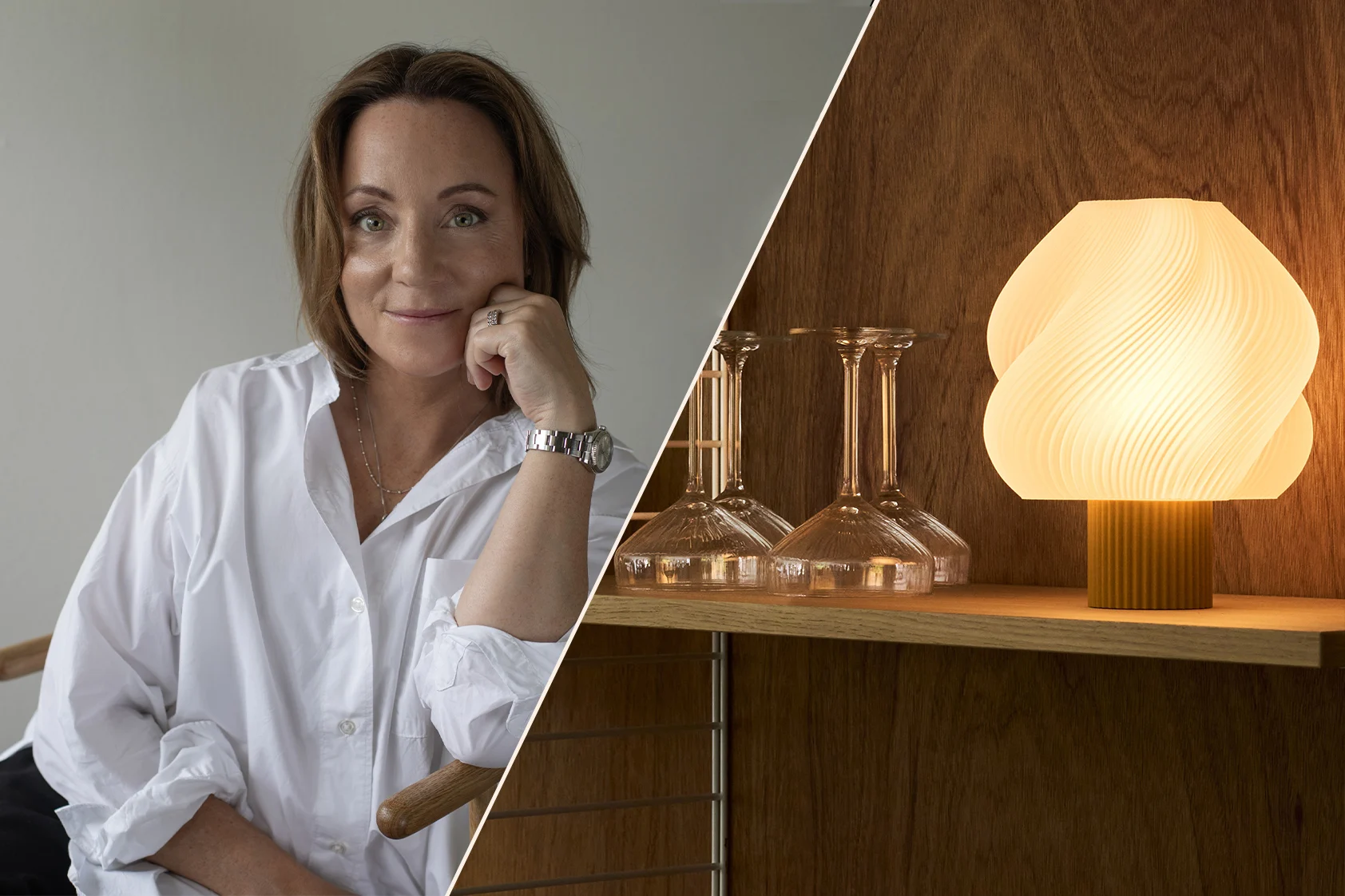 Smiling woman in a white shirt, chin on hand, wearing a watch, in a warm, modern interior with shelves and a lamp.