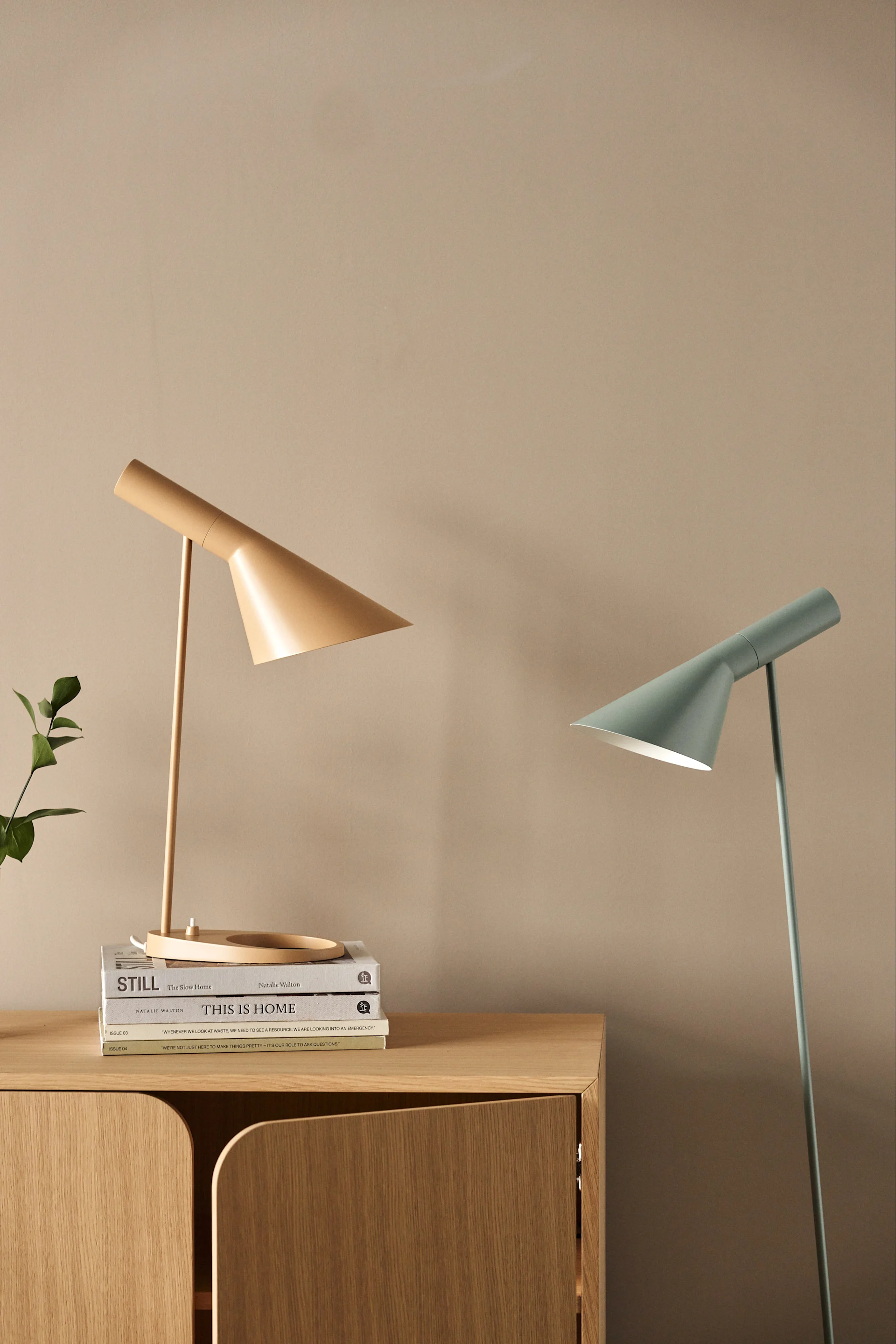 Beige table lamp on books and mint green floor lamp against a light brown wall.