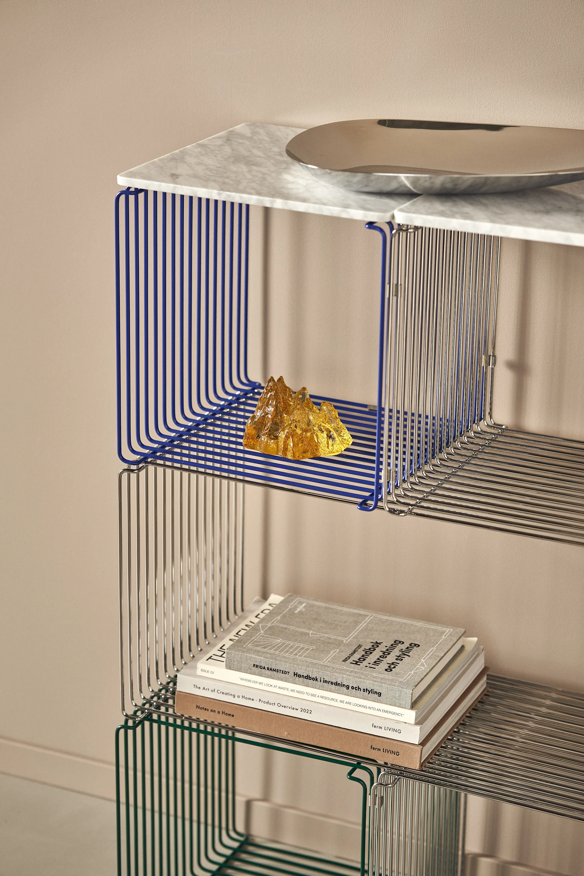 Several Panton Wire shelves from Montana are stacked to form a large shelf, decorated with The Rock candle holder and books.