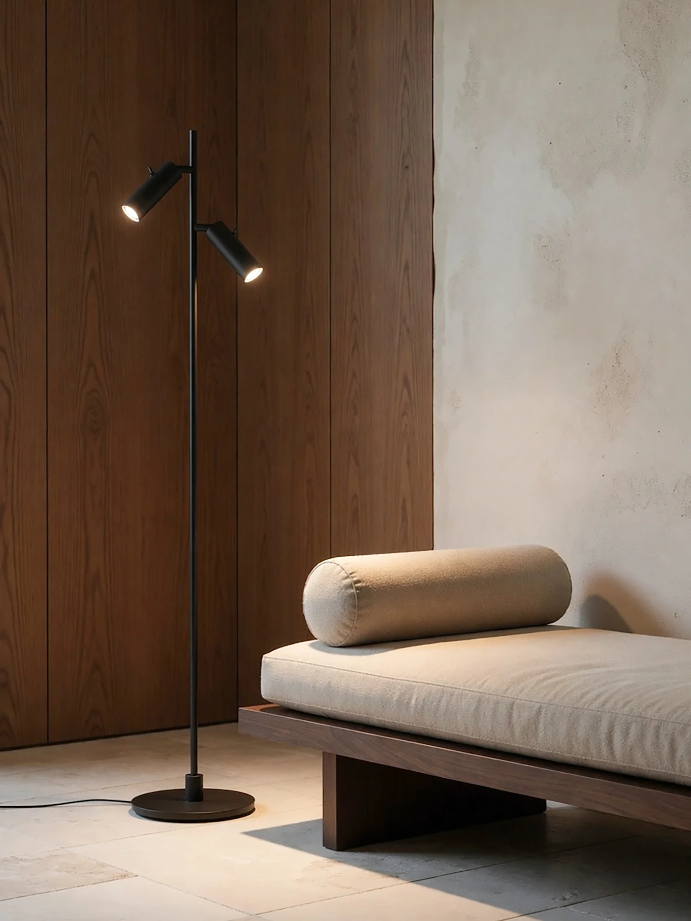 A modern room with a black two-light floor lamp next to a wood daybed with a light beige cushion and bolster.